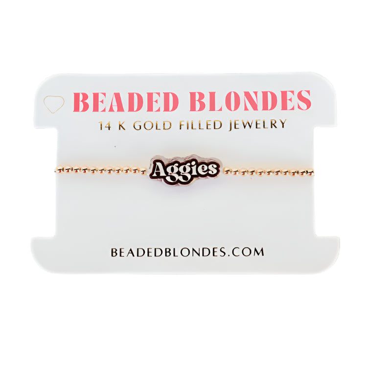 Gold bracelet with 'Aggies' charm on a 'Beaded Blondes' branded card.