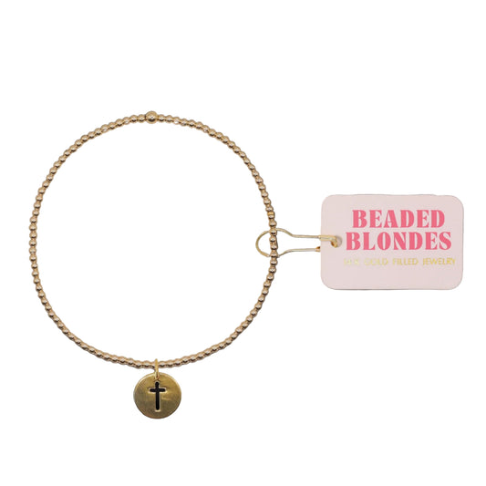 Gold beaded bracelet with a cross charm on a white background, featuring the brand 'Beaded Blondes'.